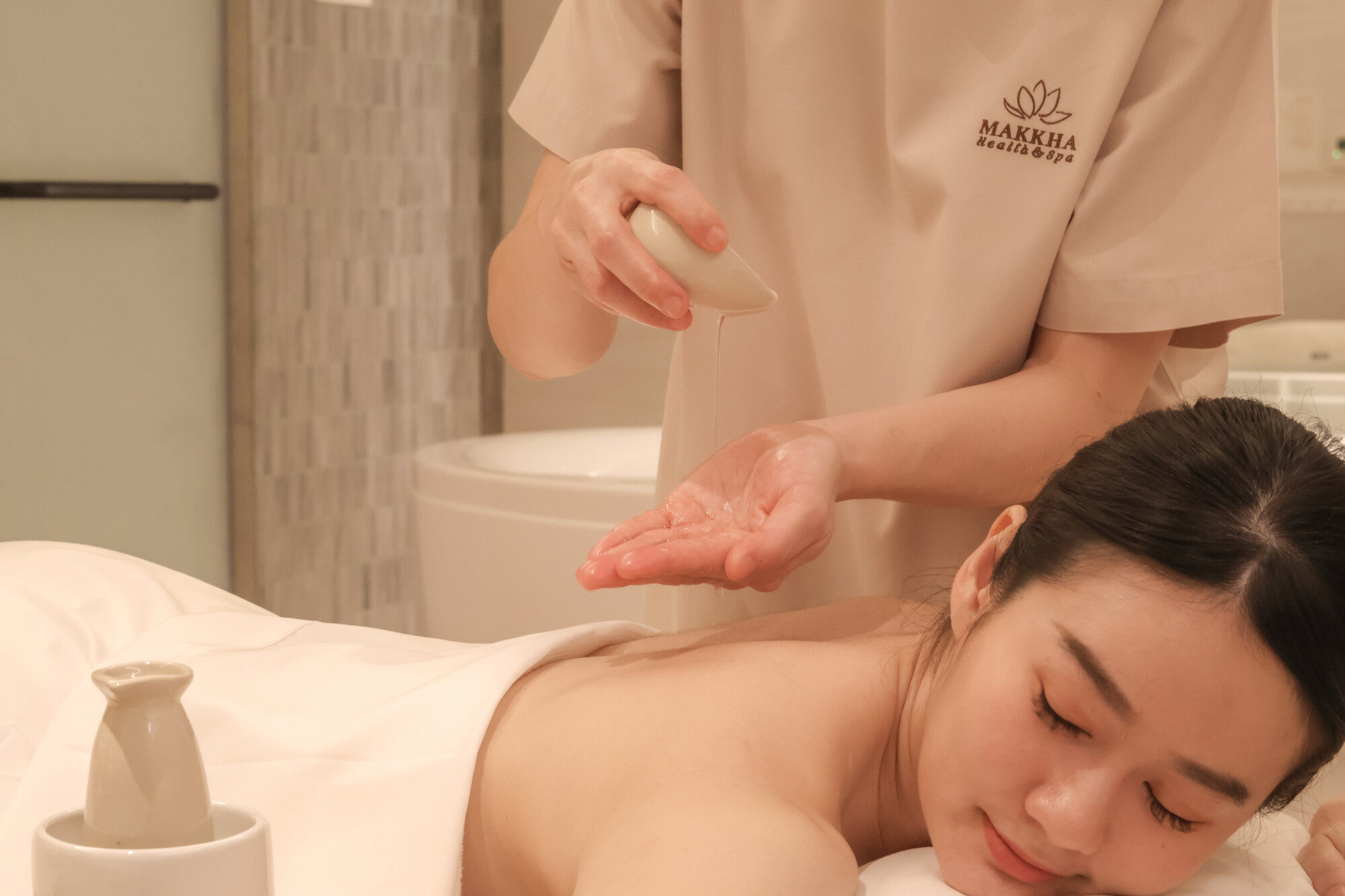 Massage therapist drips essential oils into her palm while giving an aromatherapy massage 