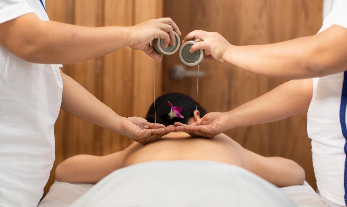 Two therapists giving a woman a hot aroma oil massage