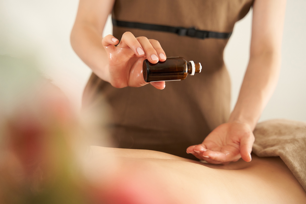 Massage therapist drips essential oils into her palm while giving an aromatherapy massage