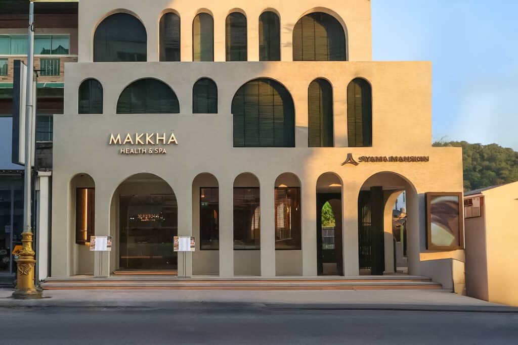 普吉島 MAKKHA 健康水療中心外觀，展示了現代拱形立面、金色招牌和毗鄰的 Syamamansion 入口。.