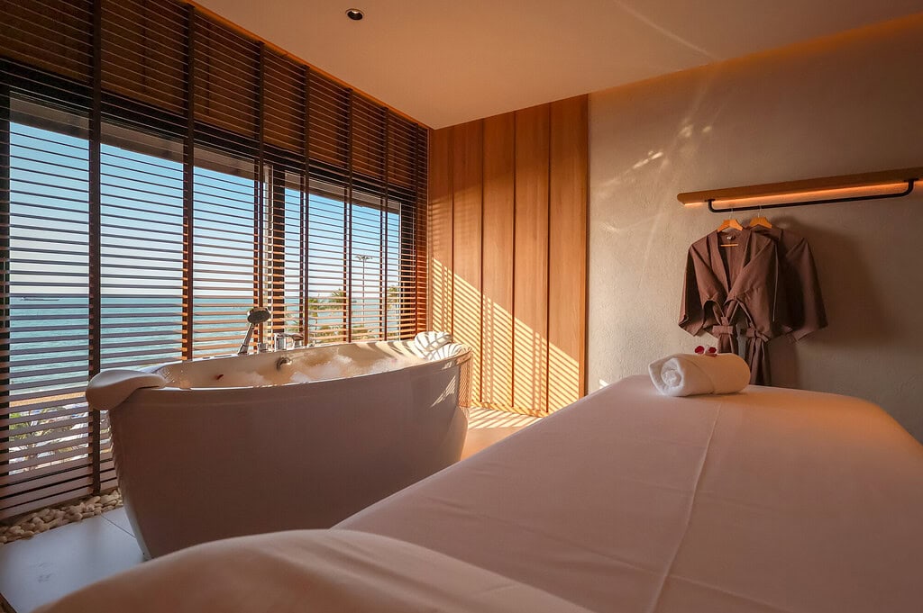 Relaxing spa treatment room with a view of Chiangmai, featuring a modern bathtub, massage bed, and wooden decor, offering a tranquil environment at Makkha Spa.