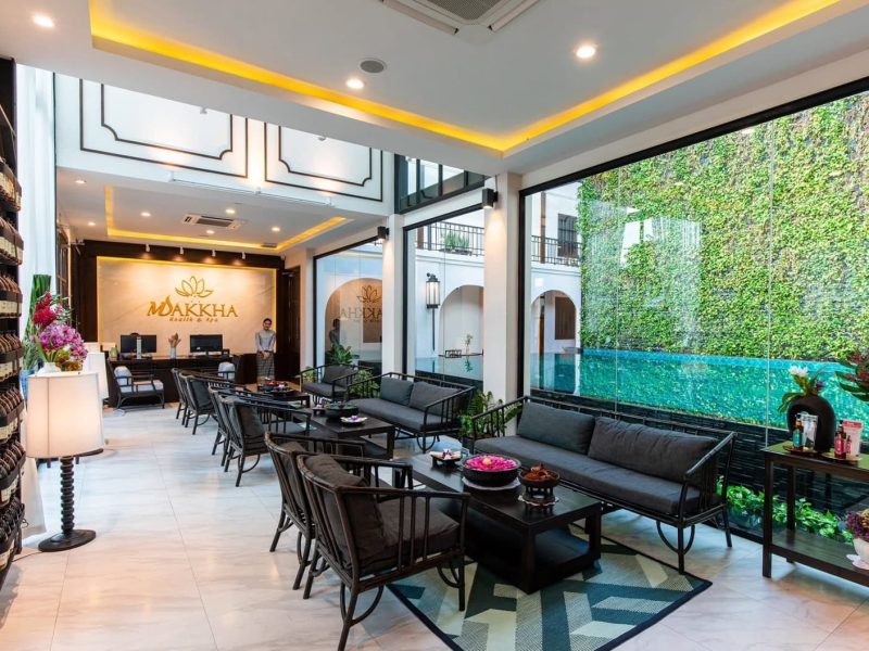 Elegant spa reception area at Makkha Spa in Chiangmai with modern decor, indoor seating, and lush outdoor pool view, offering a tranquil and luxurious wellness experience.