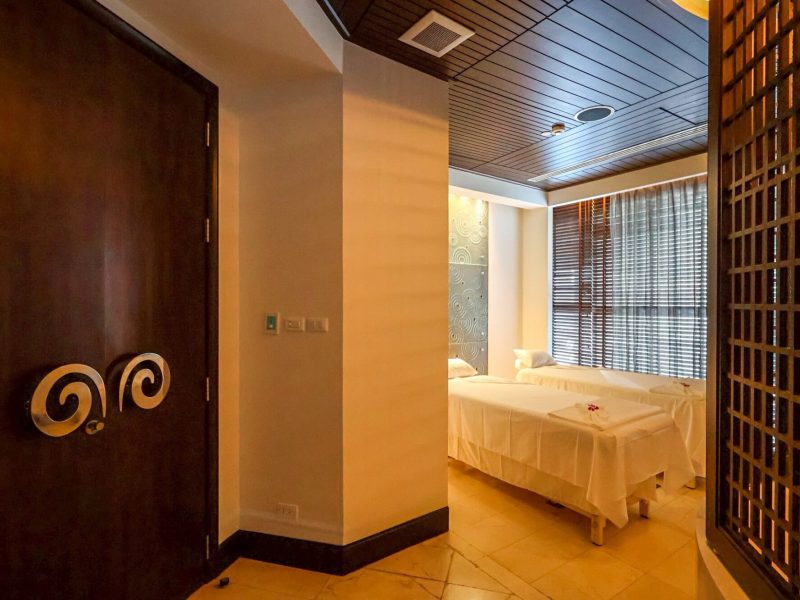 Relaxing spa treatment room with two massage beds, soft lighting, elegant decor, and large windows with wooden blinds in Chiang Mai at Makkha Spa – the best spa in Chiang Mai.