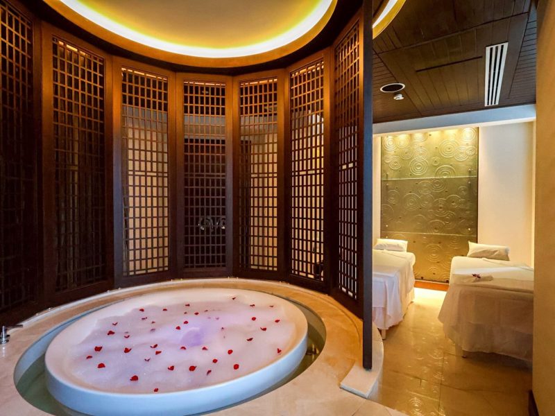 Luxurious spa treatment room with a large bubble bath decorated with rose petals, private beds, and elegant Asian-inspired wooden decor at Makkha Spa in Chiang Mai, offering the best spa experience.